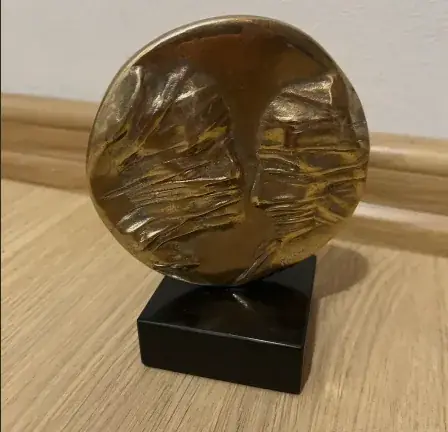 La Conversation — Igor Mitoraj, bronze medal on black marble base, three-quarter view showing warm golden patina