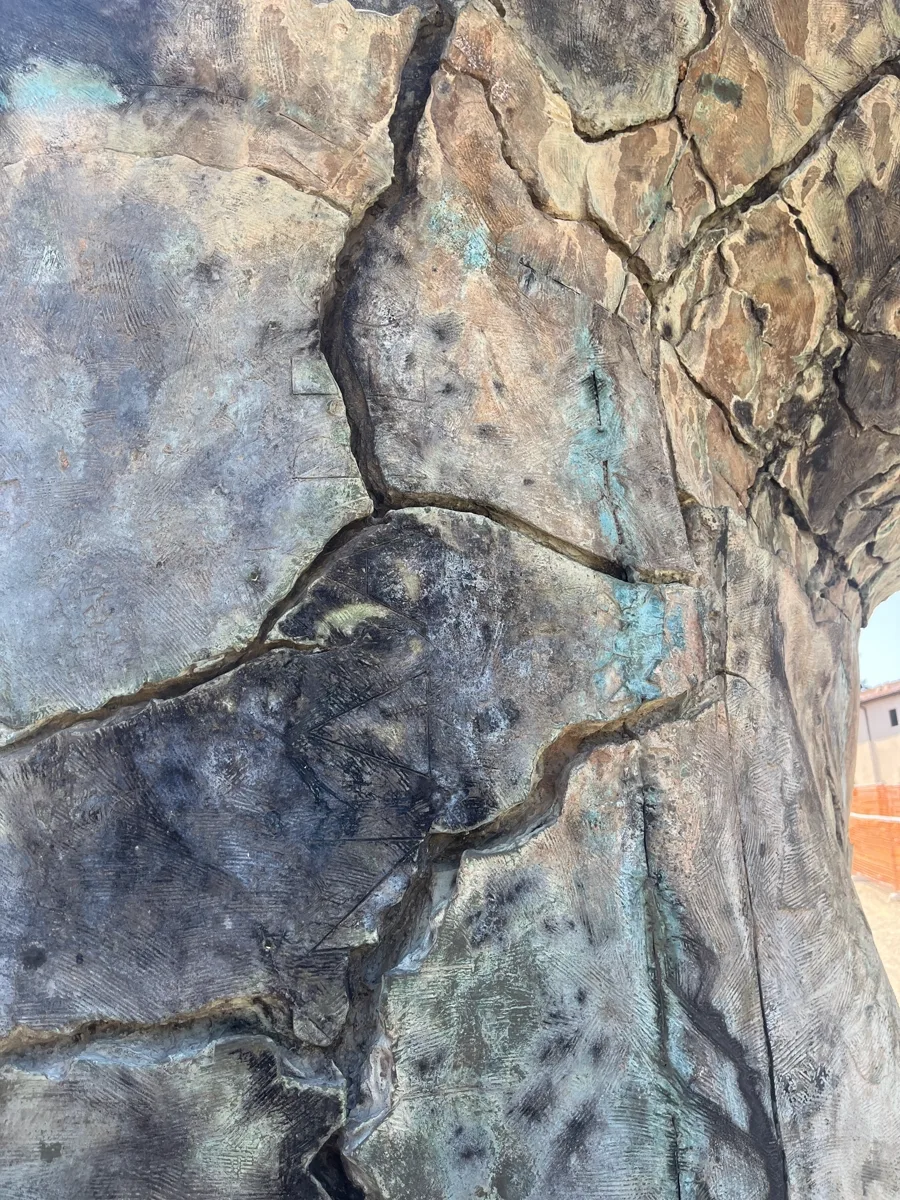 Extreme close detail of the cracked bronze surface of Tindaro Screpolato — the deliberately fractured patina in blues, greens and browns that Mitoraj used to evoke an archaeological ruin