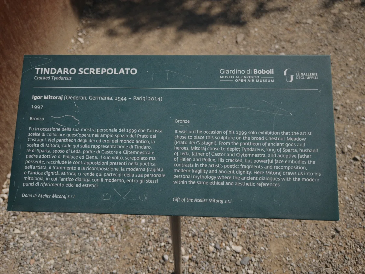 Official Uffizi Galleries information plaque at the base of Tindaro Screpolato — bilingual Italian and English text describing Igor Mitoraj's 1997 bronze donation to the Boboli Gardens