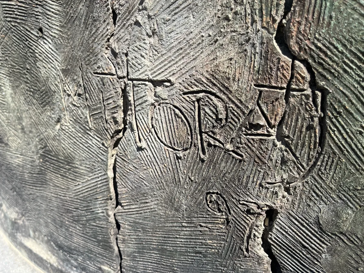 Straight-on view of the incised MITORAJ 97 signature on Tindaro Screpolato — the artist's mark cut into a smoother patch of bronze surrounded by the sculpture's characteristic cracked patina