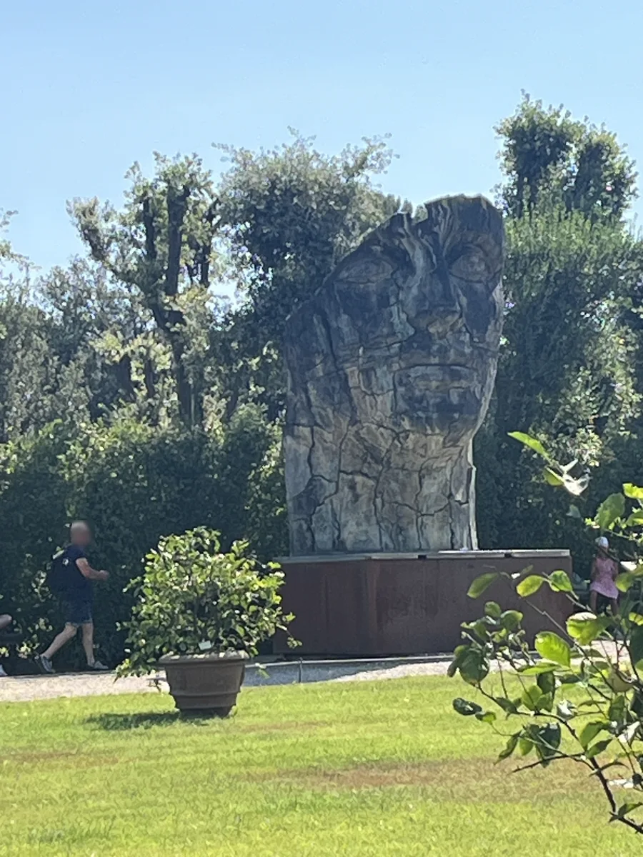 Igor Mitoraj's Tindaro Screpolato photographed from the lawn with a lone figure standing at its base — the human scale making clear the four-metre height of the bronze