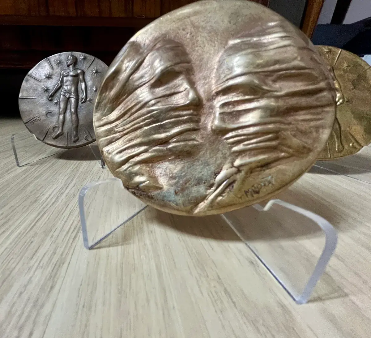 La Conversation — Igor Mitoraj, three specimens low-angle on granite: gilt reverse, worn obverse, dark reverse, acrylic stands