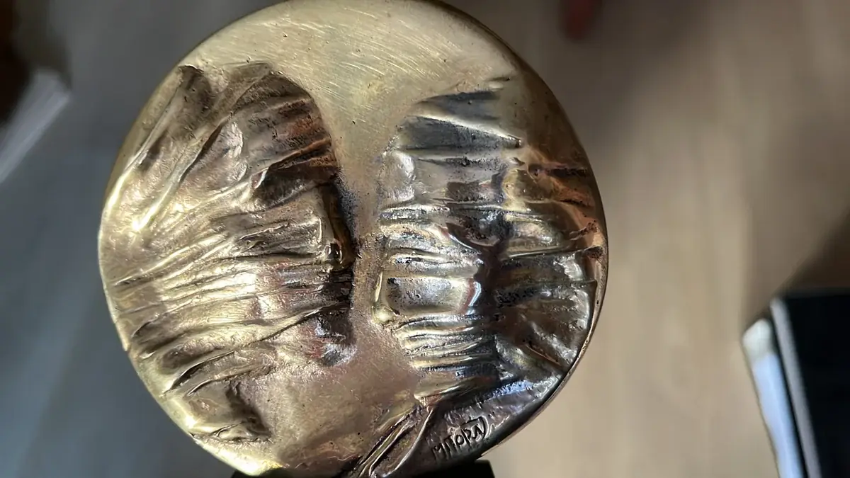 La Conversation — Igor Mitoraj, close-up of obverse: two veiled faces meeting at centre, MITORAJ signature visible, warm gold patina