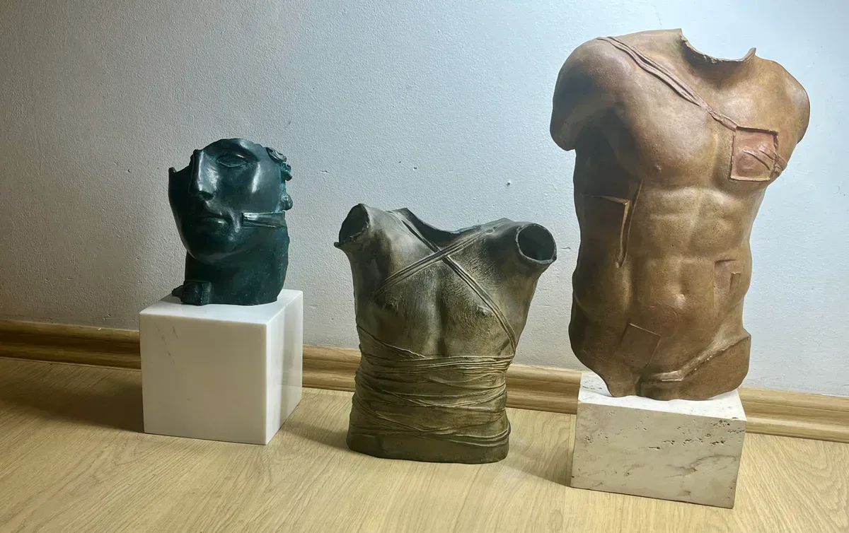 Persée (1988) — Igor Mitoraj, brown patina bronze torso shown right alongside a small green-black bronze head on marble base and a wrapped bronze torso, three-piece Mitoraj collection grouping, private collection Warsaw