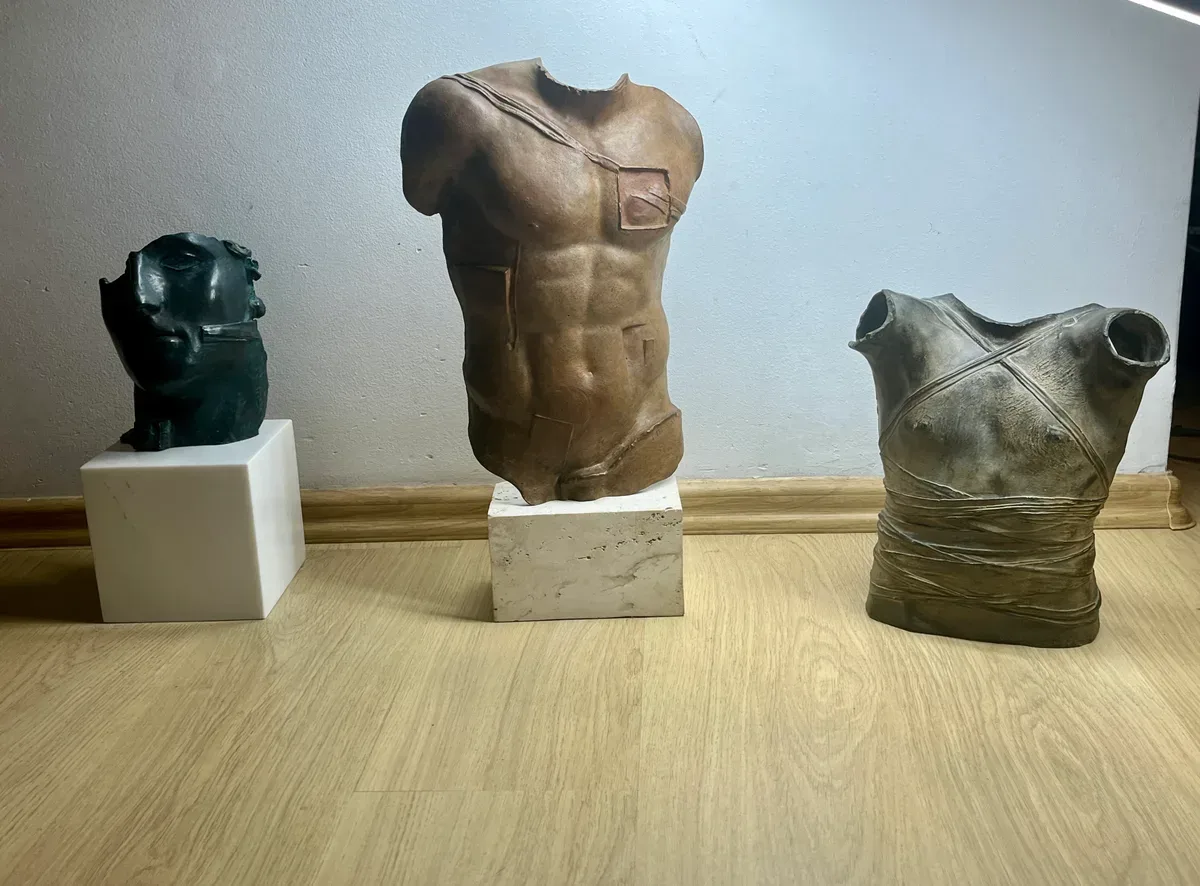 Persée (1988) — Igor Mitoraj, brown patina bronze torso central, flanked by smaller green-black bronze head on marble base and wrapped bronze torso, three-piece grouping documenting relative scale, private collection Warsaw