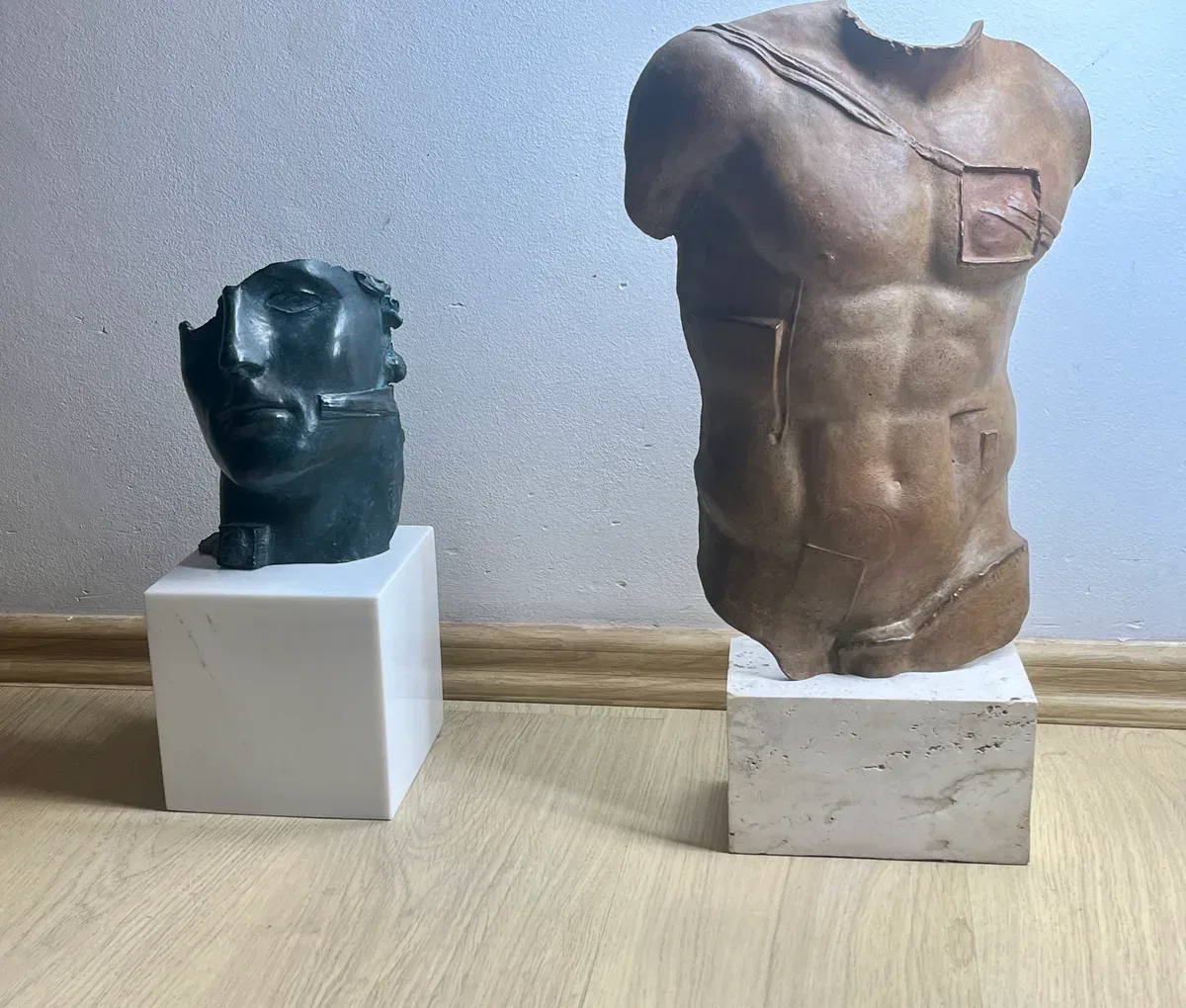 Persée (1988) — Igor Mitoraj, brown patina bronze torso displayed beside small green-black bronze head on marble base, two-piece collection pairing, scale reference visible, private collection Warsaw