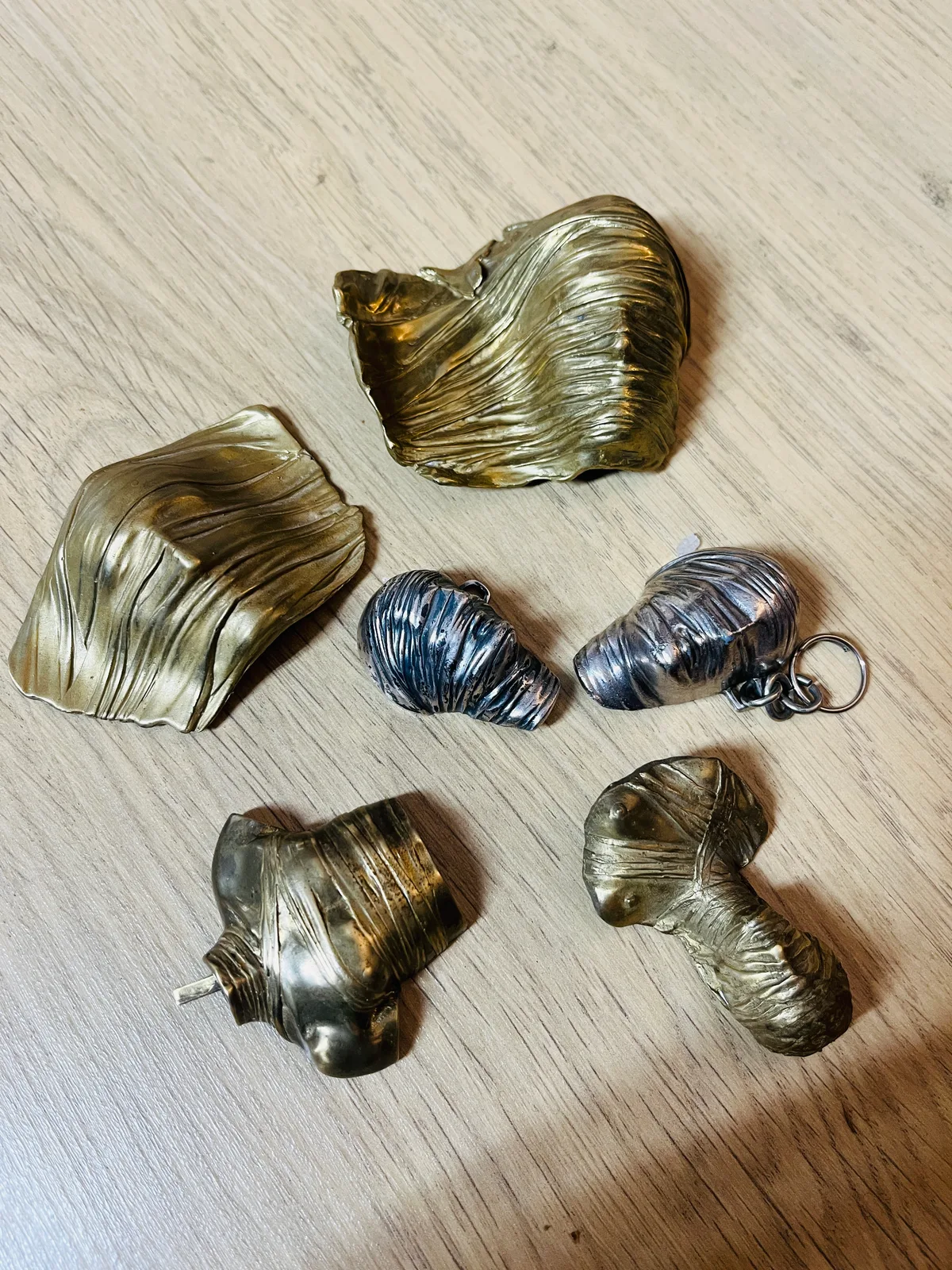 Testa Addormentata silver pair alongside Mitoraj gilt-bronze miniature wrapped-form study collection on wood surface